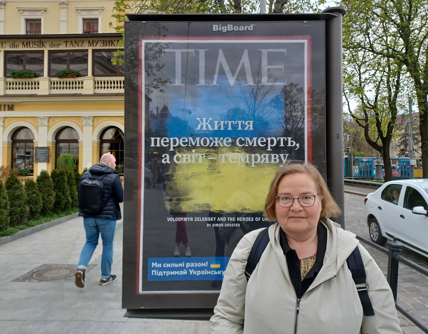 silmälasipäinen nainen mainostaulun edessä ukrainan lvivissä