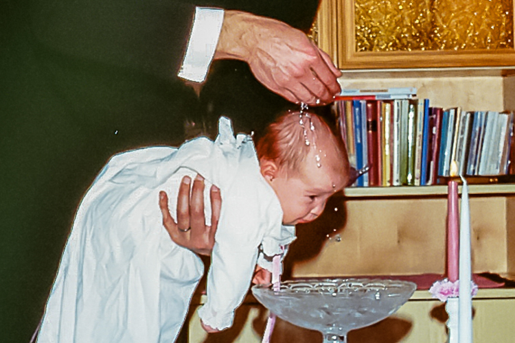 Kuvassa näkyy vauva, jota pappi on juuri kastamassa.