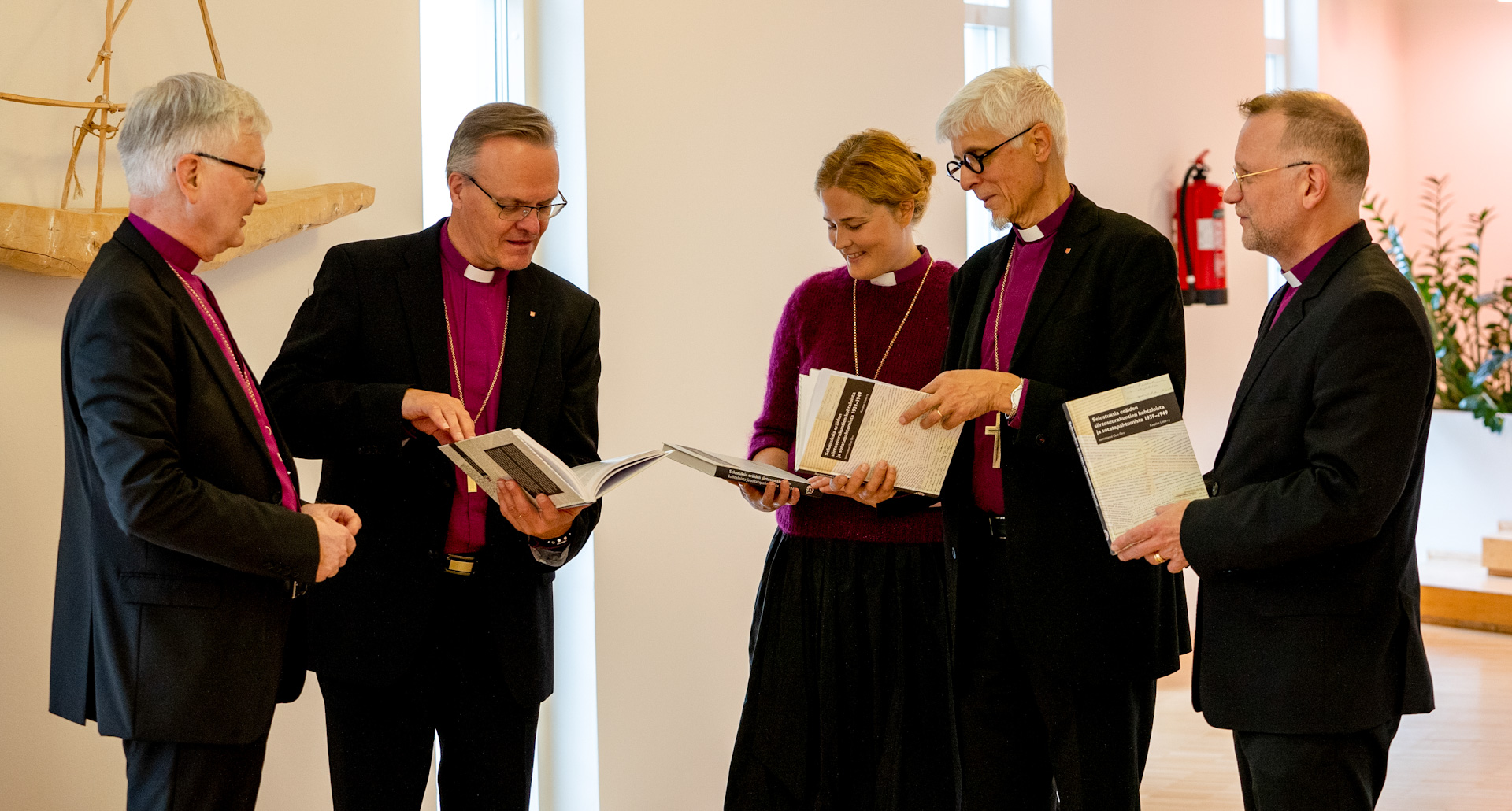 viisi piispaa, joista yksi nainen selaa kirjaa