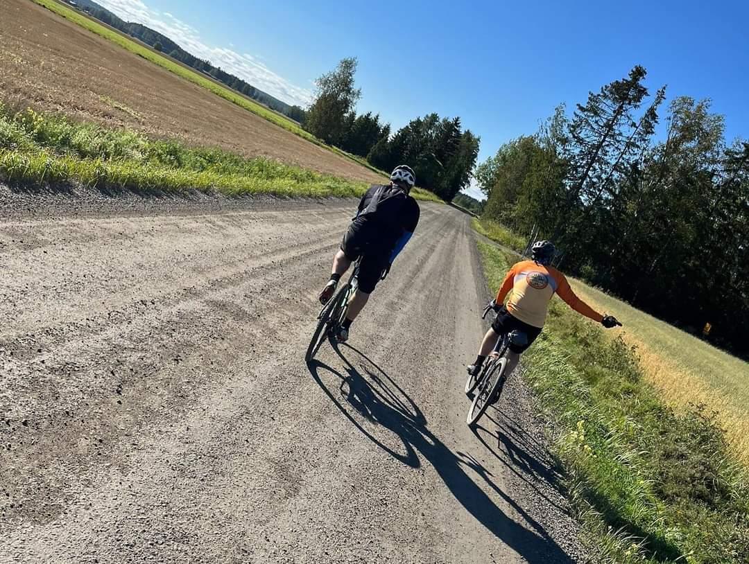 kaksi pyöräilijää maantiellä peltomaisemassa.